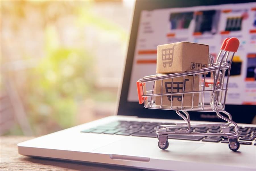 What Is White Label Ecommerce - A miniature shopping cart filled with small branded boxes placed on a laptop keyboard representing online shopping concept